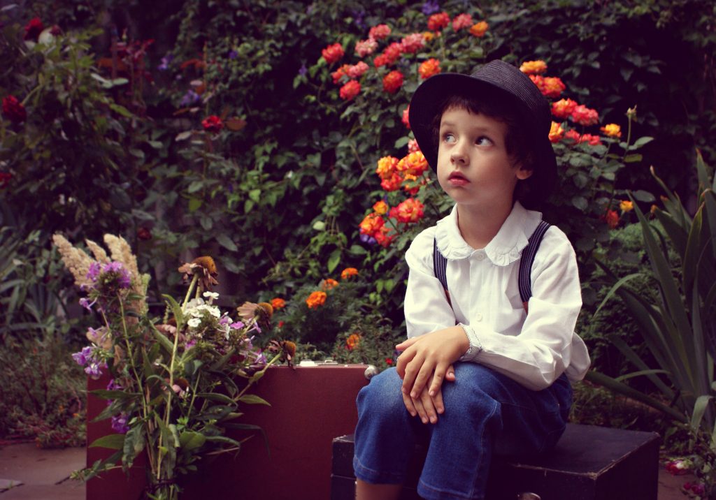 Jung mit Hut vor Blumen, ein Träumer in Gedanken versunken